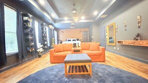 Ein Zimmer mit einer Couch, einem Hocker und einem Bett im Hintergrund.