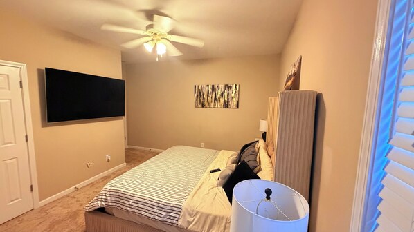 A bedroom with a bed, a ceiling fan, a flat-screen TV, a painting, and a window with blinds. - Ultra-Luxury Estate Private Gated Entry, Spa & Concierge from-Airport and games (Douglasville)