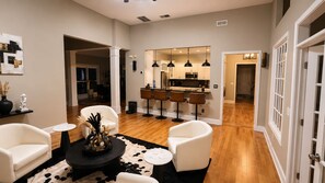 A modern living room with a fireplace, white leather chairs, a black coffee table, and a dining area with bar stools. - Ultra-Luxury Estate Private Gated Entry, Spa & Concierge from-Airport and games (Douglasville)