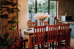 A dining area with wooden chairs and a table, a decorative fan, and a vase with dried flowers. - Stillwater Resort - Lakefront Estate with two dwellings, spa pools, SUPs - Sleeps 16 (Rotorua)