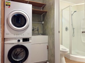 A laundry area with a front-loading washing machine and dryer, a sink with a mirror, and a glass-enclosed shower. - Stillwater Resort - Lakefront Estate with two dwellings, spa pools, SUPs - Sleeps 16 (Rotorua)