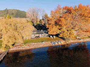 A lakeside property with a house, a dock with kayaks, and autumn foliage. - Stillwater Resort - Lakefront Estate with two dwellings, spa pools, SUPs - Sleeps 16 (Rotorua)