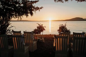 A sunset view over a calm body of water with chairs arranged facing the water, decorated with flowers.
