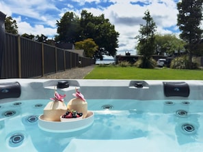 A hot tub with a tray of fruit and a view of a fenced yard and trees. - Stillwater Resort - Lakefront Estate, Sleeps 16 (Rotorua)