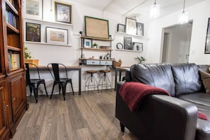 Ein Wohnzimmer mit einer Ledersofa, einem Holzschrank, einem Schreibtisch mit zwei Stühlen und einem Bücherregal.
