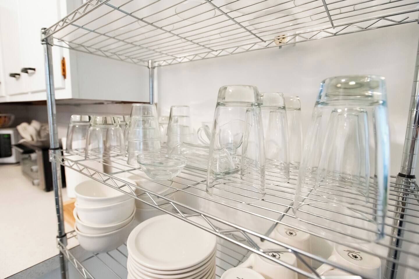 A metal shelf with clear glassware and stacked white plates.