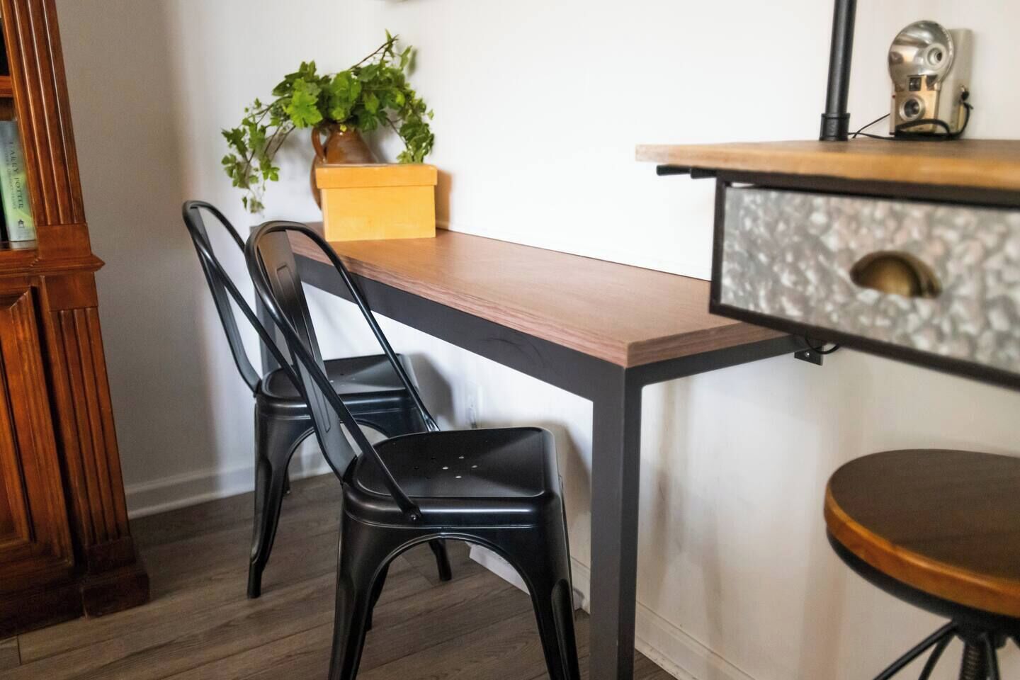 A dining area with a wooden table, black chairs, a potted plant, and a small cabinet with a decorative handle.