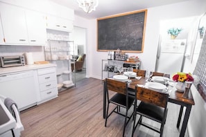 Eine moderne Küche mit weißen Schränken, ein Essbereich mit Holzsesseln und einer Tafel an der Wand.