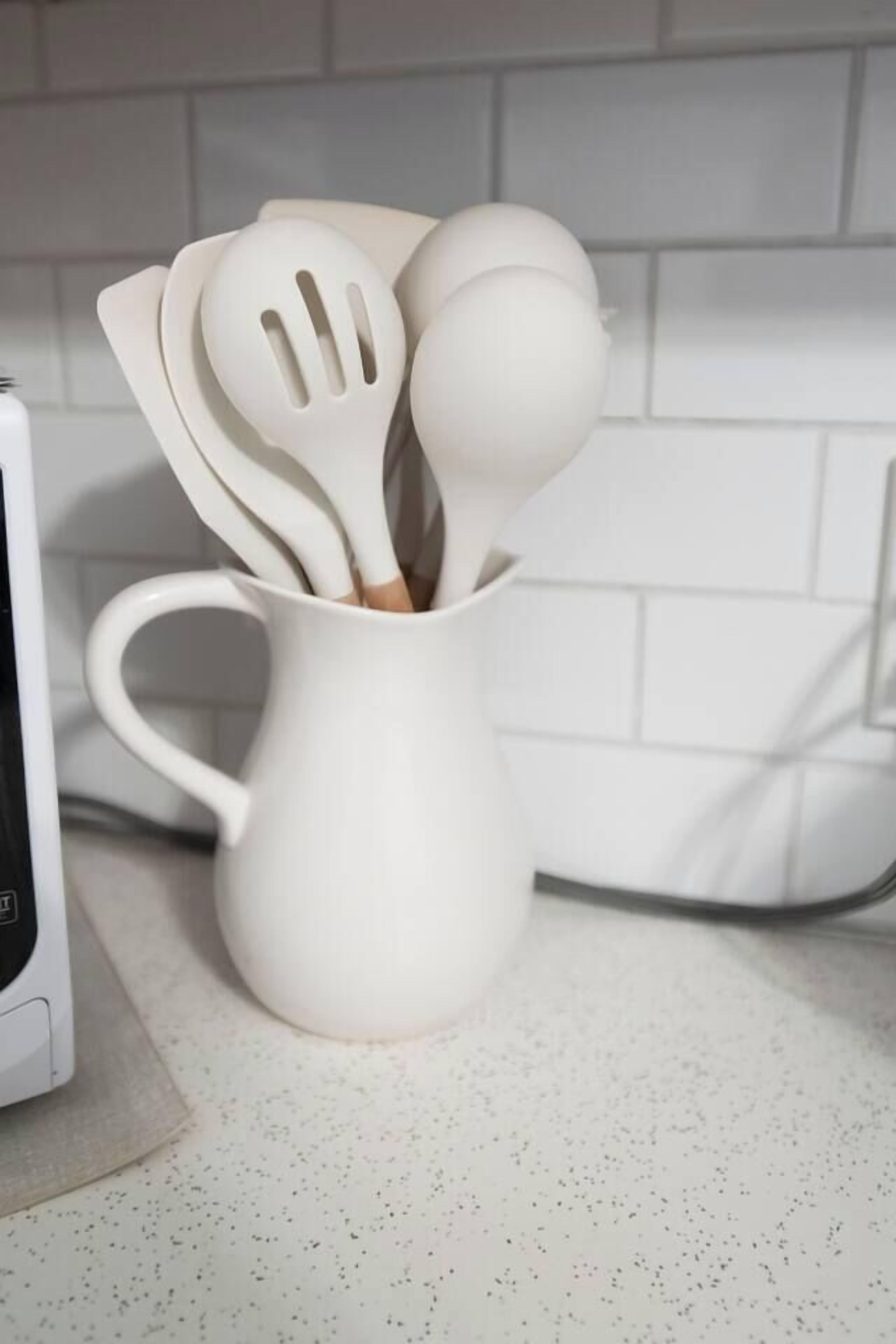 Un porte-ustensiles de cuisine blanc, contenant des spatules et une louche, posé sur un plan de travail à motifs.