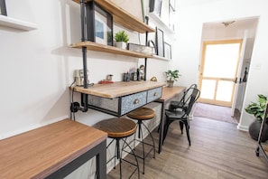 Una cocina con mostrador de madera, taburetes de bar y una estantería empotrada con plantas y utensilios de cocina.