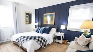 Quarto bem arrumado com cama, mesas de cabeceira, abajur e janela com persianas.