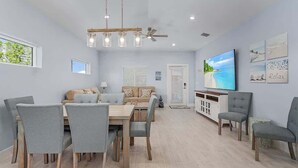 A dining area with a table and chairs, a sofa, a TV, and artwork on the wall. - Beach Time  - Elevator - Pool - 3 Min to Beach (Fort Myers Beach)