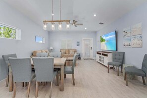 A dining area with a table and chairs, a sofa, a TV, and artwork on the wall. - Beach Time  - Elevator - Pool - 3 Min to Beach (Fort Myers Beach)