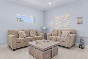 A living room with two beige sofas, a wooden coffee table, a side table with a lamp, and a decorative item. - Beach Time  - Elevator - Pool - 3 Min to Beach (Fort Myers Beach)