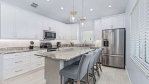 A modern kitchen with white cabinets, stainless steel appliances, a granite countertop, and bar stools. - Beach Time  - Elevator - Pool - 3 Min to Beach (Fort Myers Beach)