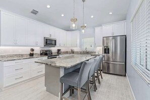 A modern kitchen with white cabinets, stainless steel appliances, a granite countertop, and bar stools. - Beach Time  - Elevator - Pool - 3 Min to Beach (Fort Myers Beach)