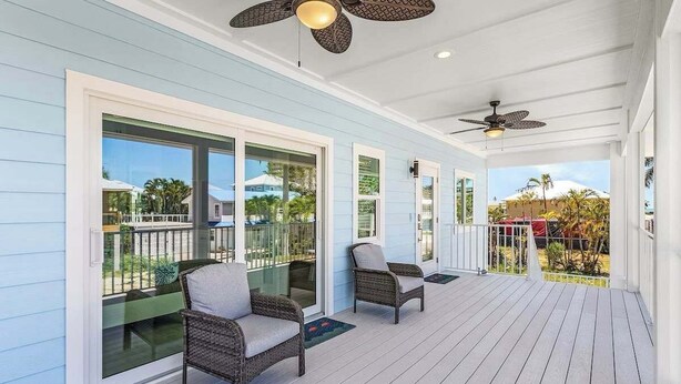 A covered porch with two wicker chairs, large windows, and ceiling fans. - Beach Time  - Elevator - Pool - 3 Min to Beach (Fort Myers Beach)