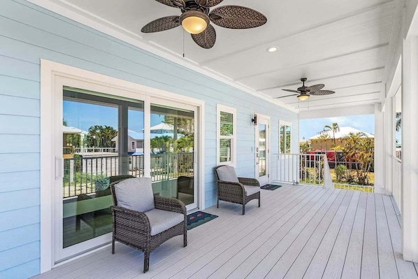 A covered porch with two wicker chairs, large windows, and ceiling fans. - Beach Time  - Elevator - Pool - 3 Min to Beach (Fort Myers Beach)
