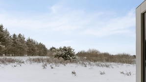 Schneebedeckte Landschaft mit Baum und Gebäude im Vordergrund.