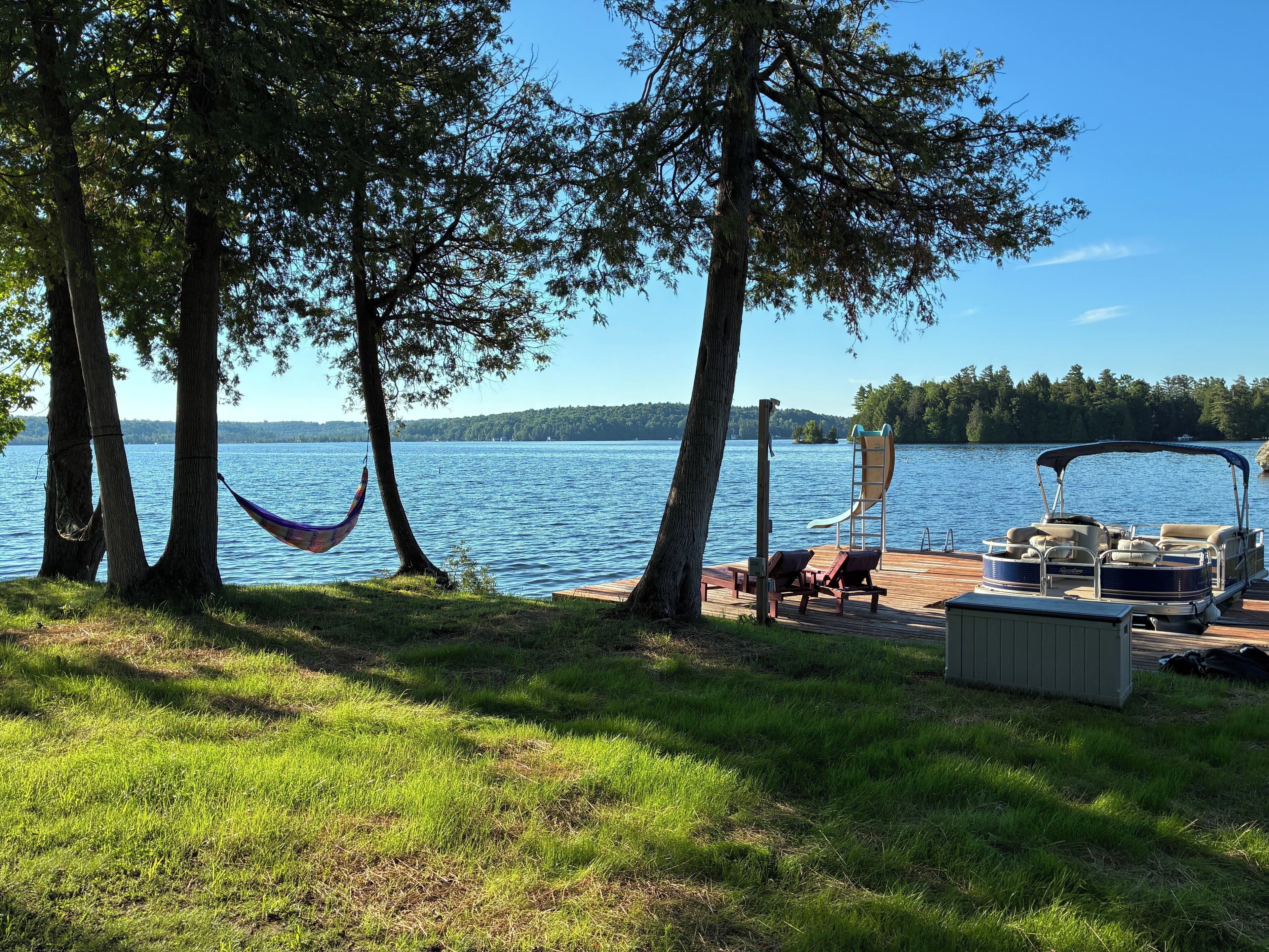 Une terrasse au bord du lac, avec un hamac, des chaises longues et un quai pour bateaux.
