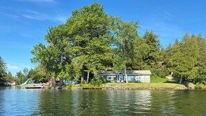 Ein Seehäuschen mit Steg, umgeben von Bäumen und blauem Himmel.