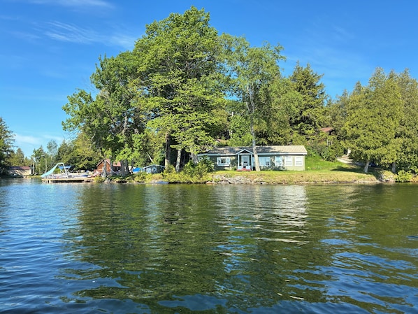 A lakeside cabin with a dock, surrounded by trees and a clear sky.