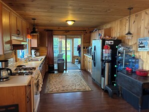A wooden cabin kitchen with a stove, sink, refrigerator, and a water dispenser.