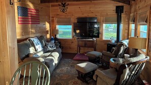 Ein Interieur einer Holzhütte mit einer Couch, Sesseln, einem Tisch, einem Fernseher und einem Kamin.