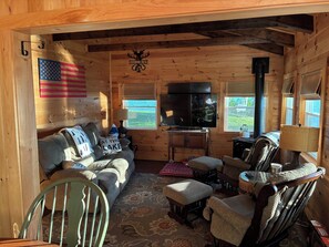 Un interior de cabaña con sofá, sillas, una mesa, televisor y chimenea.