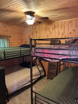 Camera con letto a castello, ventola a soffitto, pareti in legno e finestra con tende.