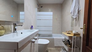 Un baño con lavamanos, inodoro, ducha y un perchero para toallas.