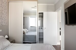A modern bedroom with a bed, a nightstand, a wardrobe, and a television. - Flat Moderno Proximo ao Aeroporto (São Paulo)