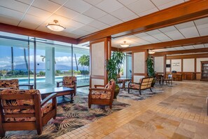 Eine geräumige Lobby mit Blick auf den Pool, Holzmöbel und einem tropisch gestalteten Teppich.