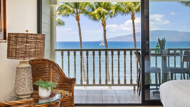 Varanda com vista para o oceano, uma cadeira de vime, uma mesa com vaso e planta, e uma cama.