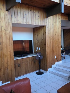 A room with wooden panel walls, a flat-screen TV, a standing fan, and a staircase leading to an upper level. - Spacious 6-bedroom 4 toilets house in Houston Texas  available for short rent (Houston)