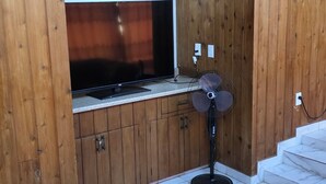 Quarto com armário de madeira, televisão, ventilador e sofá vermelho.