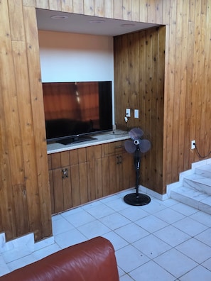 A room with a wooden cabinet, a television, a fan, and a red couch. - Spacious 6-bedroom 4 toilets house in Houston Texas  available for short rent (Houston)