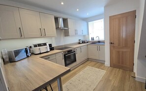 A modern kitchen with light-colored cabinets, a built-in oven, a microwave, and a coffee machine.