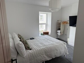 A bedroom with a bed, a window, a TV, and a towel rack. - Modern 3 Bed Home | Near Sellafield & The Fells (Cumberland)