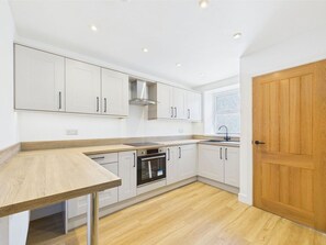 Una cocina moderna con armarios blancos, encimera de madera y horno empotrado.
