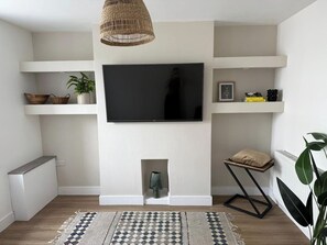 Una sala de estar moderna con un televisor de pantalla plana sobre la chimenea, suelo de madera y una alfombra estampada.