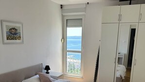 A bedroom with a bed, a wardrobe, a window with a view, and a painting on the wall. - 2BR Sea View | 3 ACs | Žnjan Walk (Split)