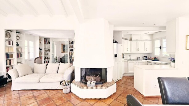 Een woonkamer met een witte bank, een open haard en een keuken met witte kastjes.