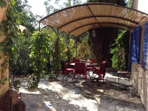 An outdoor patio with stone flooring, red metal chairs, a round table, and a straw canopy. - Charming Provençal villa with a pool and sauna (MONTFERRAT)