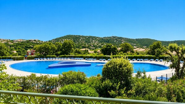 Ein großer, runder Pool mit einer zentralen Insel, umgeben von Liegestühlen und Pflanzen, mit hügeliger Landschaft im Hintergrund.