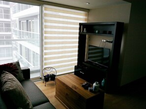 A living room with a sofa, a wooden coffee table, a TV on a stand, a window with blinds, and a balcony view. - Your Furnished Apartment on Pardo Avenue, Miraflores, Lima – Excellent Location (Miraflores)