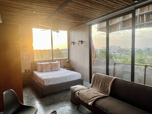 A bedroom with a bed, a sofa, a chair, a large window, and a ceiling fan. - Cozy studio with sunset view in lovely Tulum with AC (Tulum)