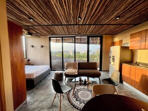 A modern room with a bed, a sofa, a dining table with chairs, a kitchen area, and large windows offering a city view. - Cozy studio with sunset view in lovely Tulum with AC (Tulum)