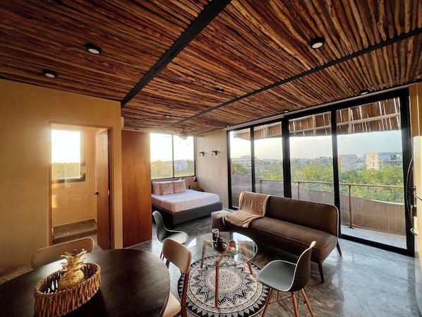 Ein modernes Zimmer mit Bett, Sofa, Esstisch und einem großen Fenster mit Blick auf die Stadt.