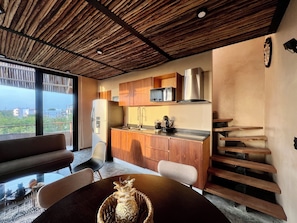 Eine moderne Küche mit Holzausbau, einem Edelstahlkühlschrank und einer integrierten Mikrowelle. Ein Essbereich mit rundem Tisch und Stühlen, sowie eine Treppe mit Holzstufen.
